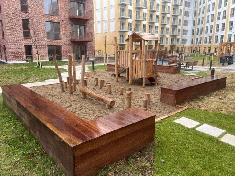 Moderne legeplads mellem boligbygninger i træ og sand